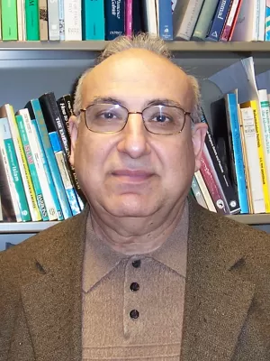 Mustansir米尔(头)戴眼镜,棕色的夹克,和棕色的衬衫,面带微笑