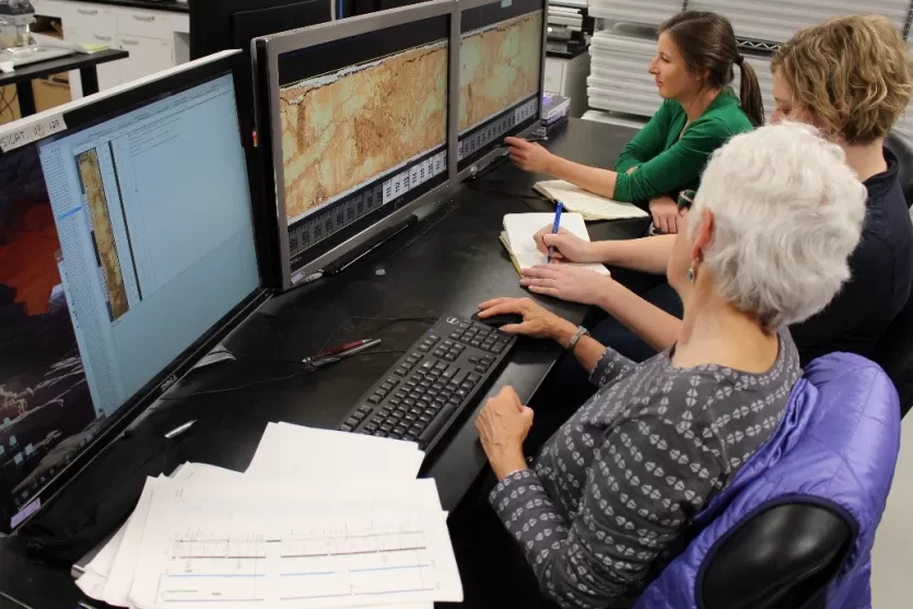 三个科学家坐下来看着电脑显示器显示放大的岩心图像部分