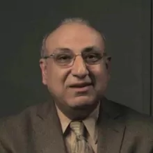 Mustansir米尔博士从肩膀说,戴眼镜,一个棕色的夹克,棕褐色的衬衫,和褐色领带